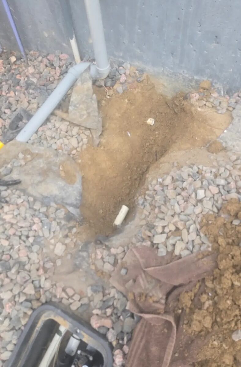 Careful hand digging at the foundation to reach a buried main line without damaging what's around it.