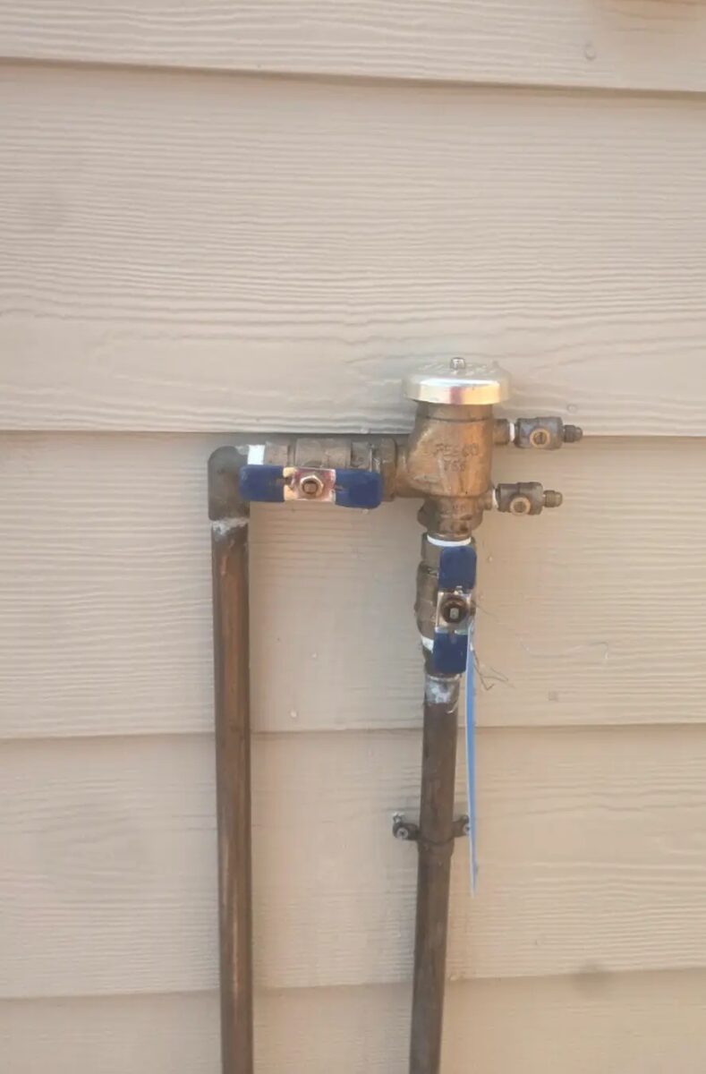 Copper riser and brass backflow assembly set square against the house with isolation valves.
